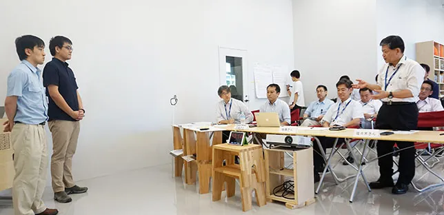 立って説明する3人のメンバーに、長机に着いた参加者たちが耳を傾けている様子